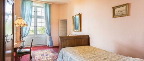 A bedroom with a bed, a desk, a chair, a lamp, and a window with curtains.