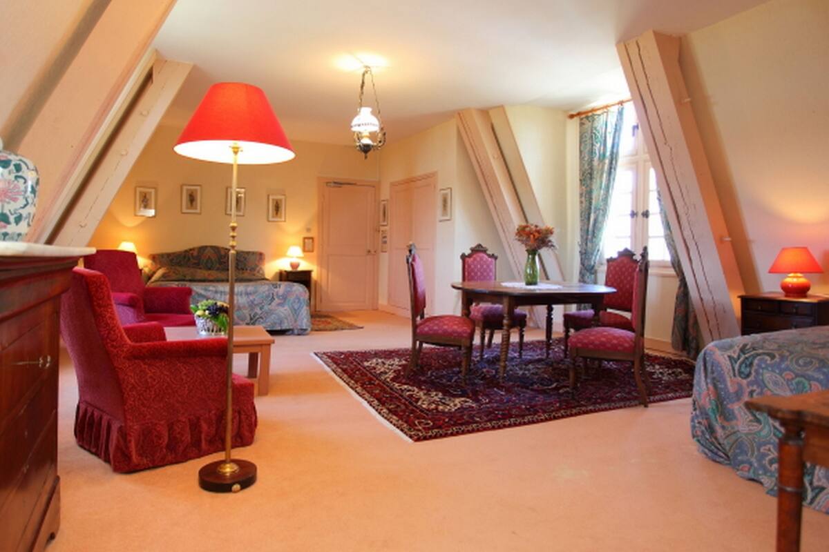 Une pièce confortable avec un lit, un fauteuil rouge, une petite table et une lampe.