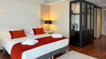 A modern hotel room with a large bed, a wardrobe, a bedside table with a lamp, and a coffee machine.