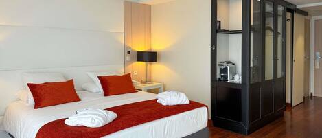 Ein modernes Hotelzimmer mit einem großen Bett, einem Kleiderschrank, einem Nachttisch mit Lampe und einer Kaffeemaschine.