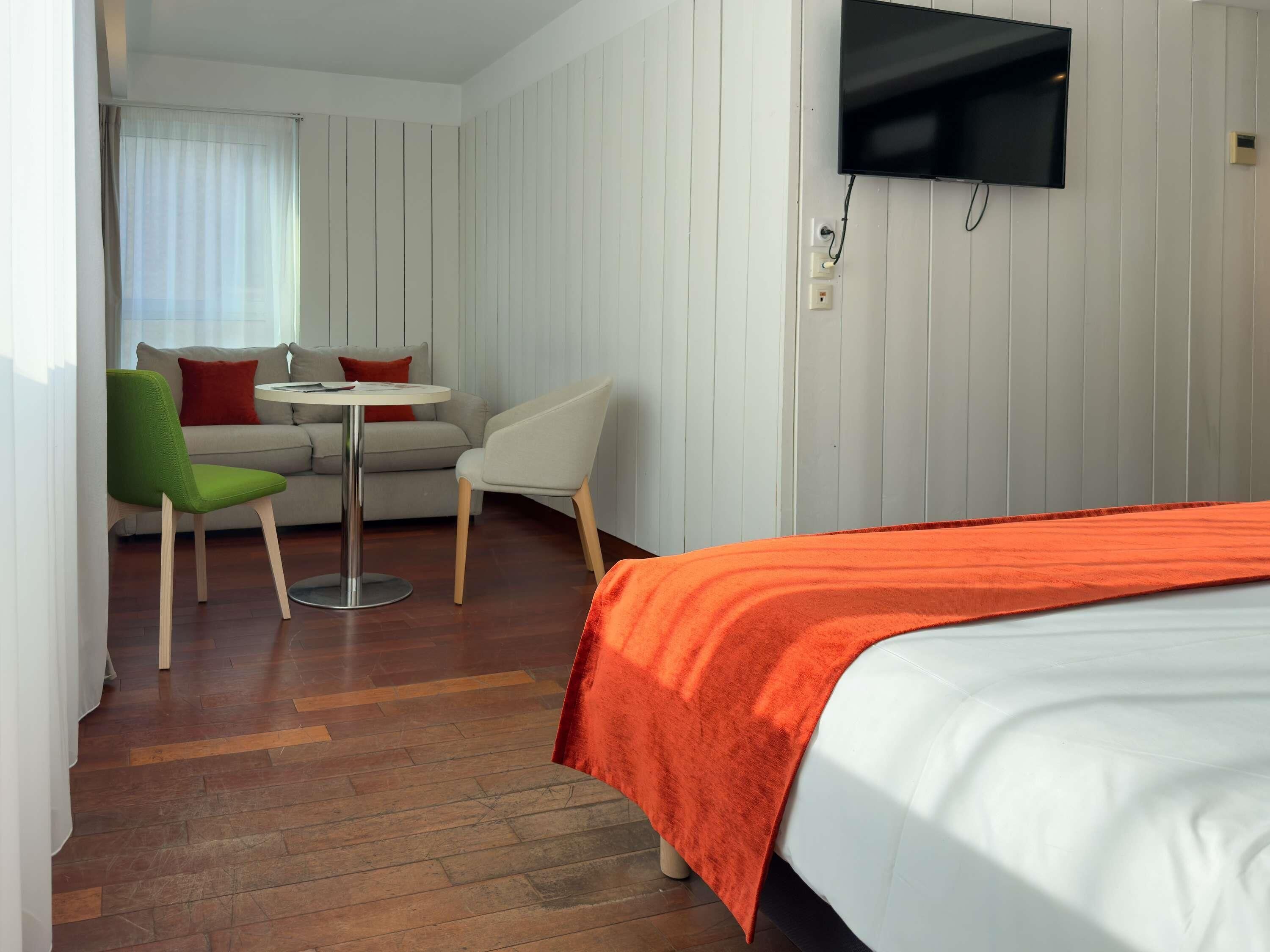 A hotel room with a bed, a TV mounted on the wall, a small round table, and two chairs.