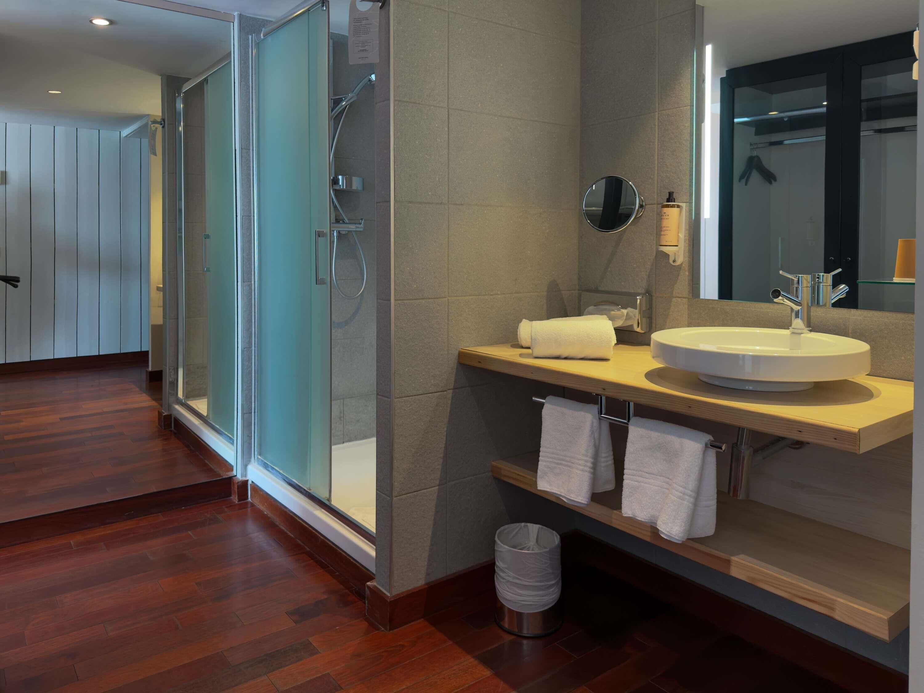 A modern bathroom with a glass shower enclosure, a sink with a mirror, and a wooden vanity.