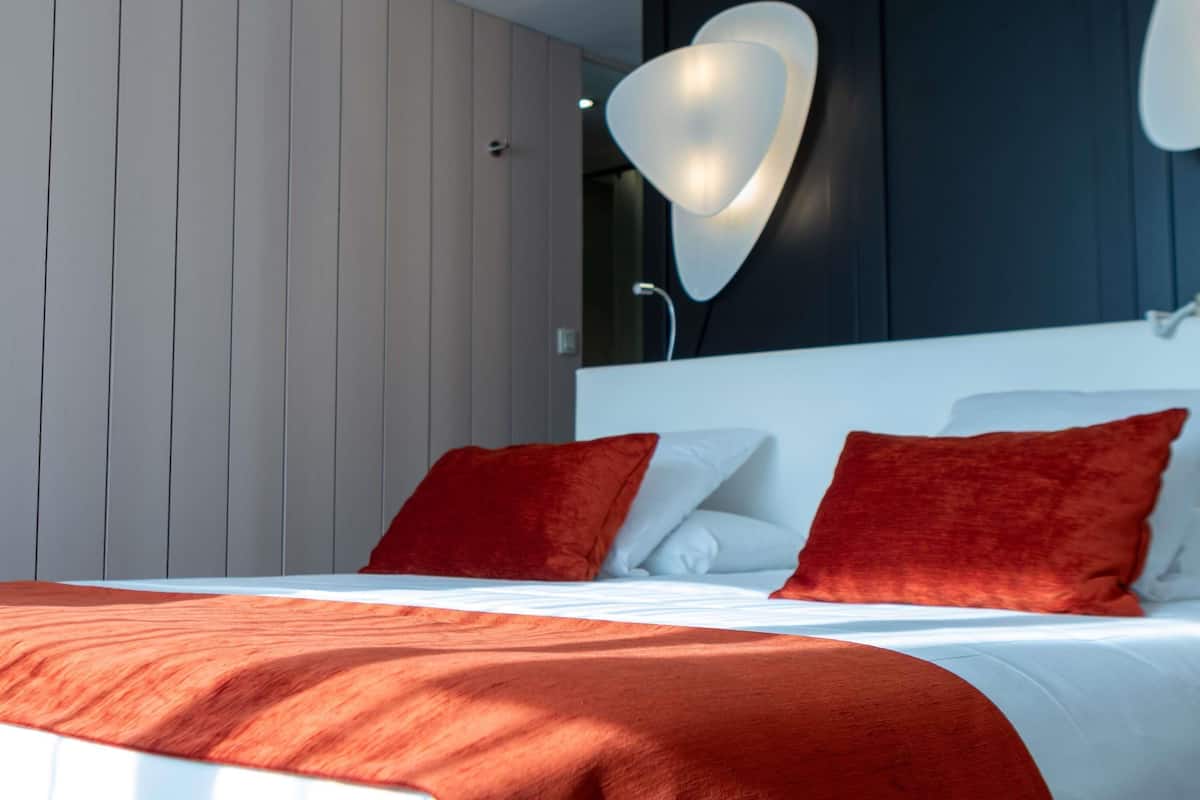 Un dormitorio moderno con una cama, almohadas rojas y una lámpara de pared original.