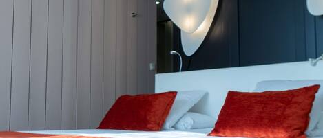 A modern bedroom with a bed, red pillows, and a unique wall-mounted light fixture.