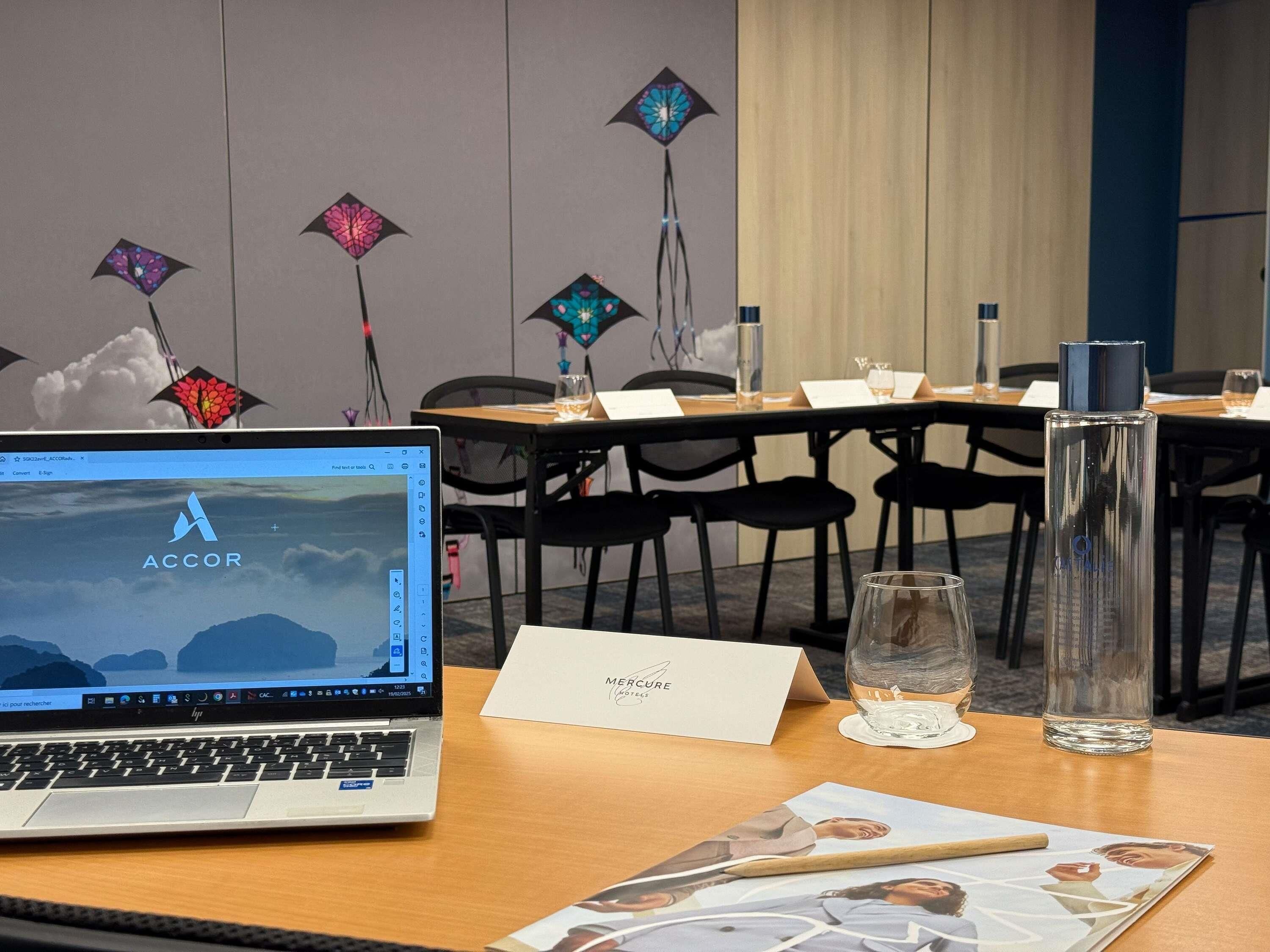 A hotel room with a laptop on a desk, a glass of water, a menu, and a decorative wall with hanging lights.