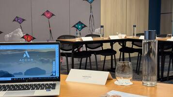 A hotel room with a laptop on a desk, a glass of water, a menu, and a decorative wall with hanging lights.