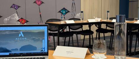 A hotel room with a laptop on a desk, a glass of water, a menu, and a decorative wall with hanging lights.