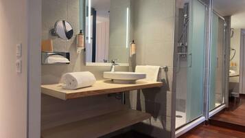Un baño moderno con cabina de ducha de vidrio, tocador de madera y un espejo grande.