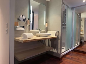 Un baño moderno con cabina de ducha de vidrio, tocador de madera y un espejo grande.