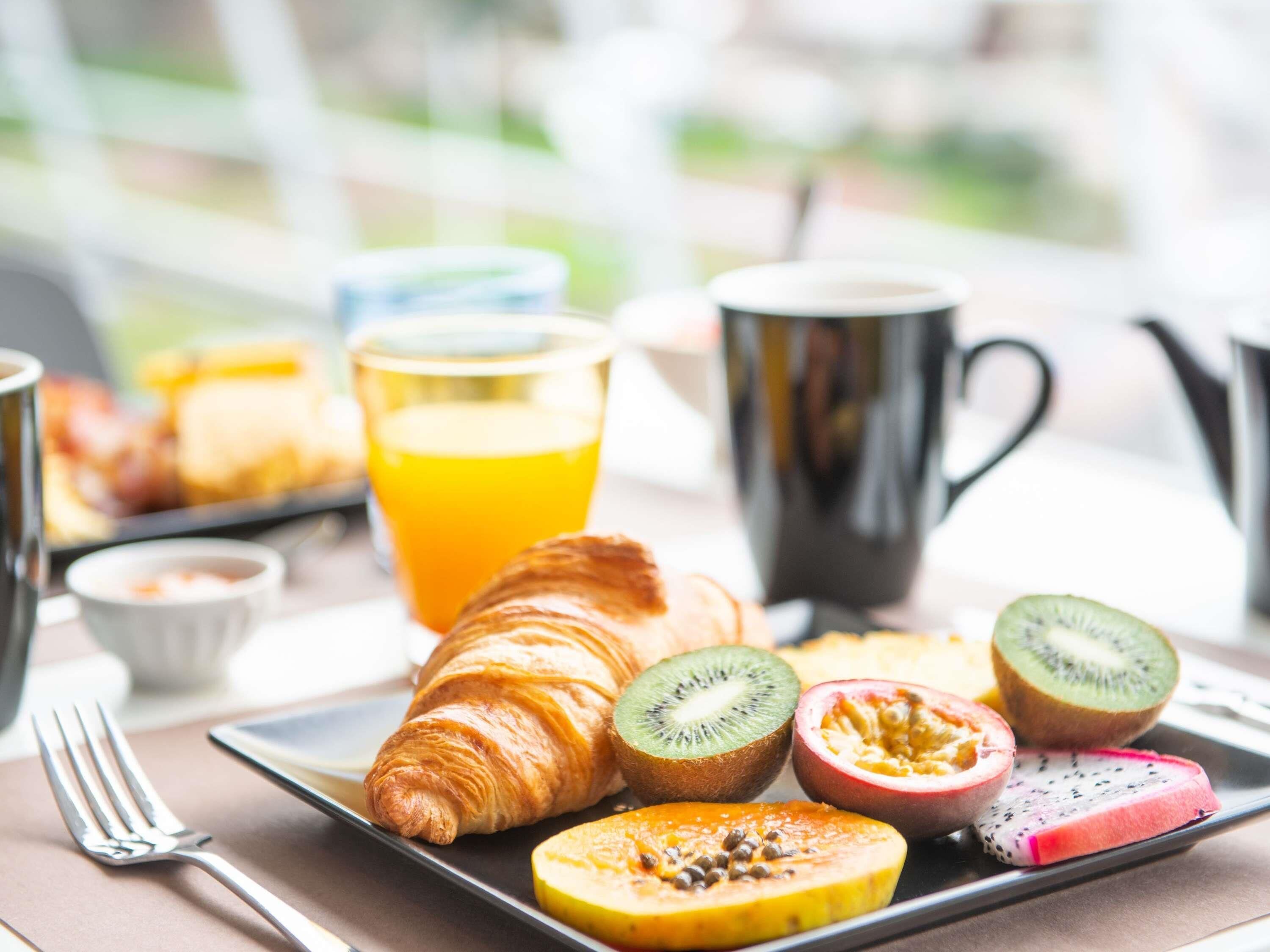 Un plato de desayuno con croissant, kiwi, papaya, pitahaya y jugo de naranja.