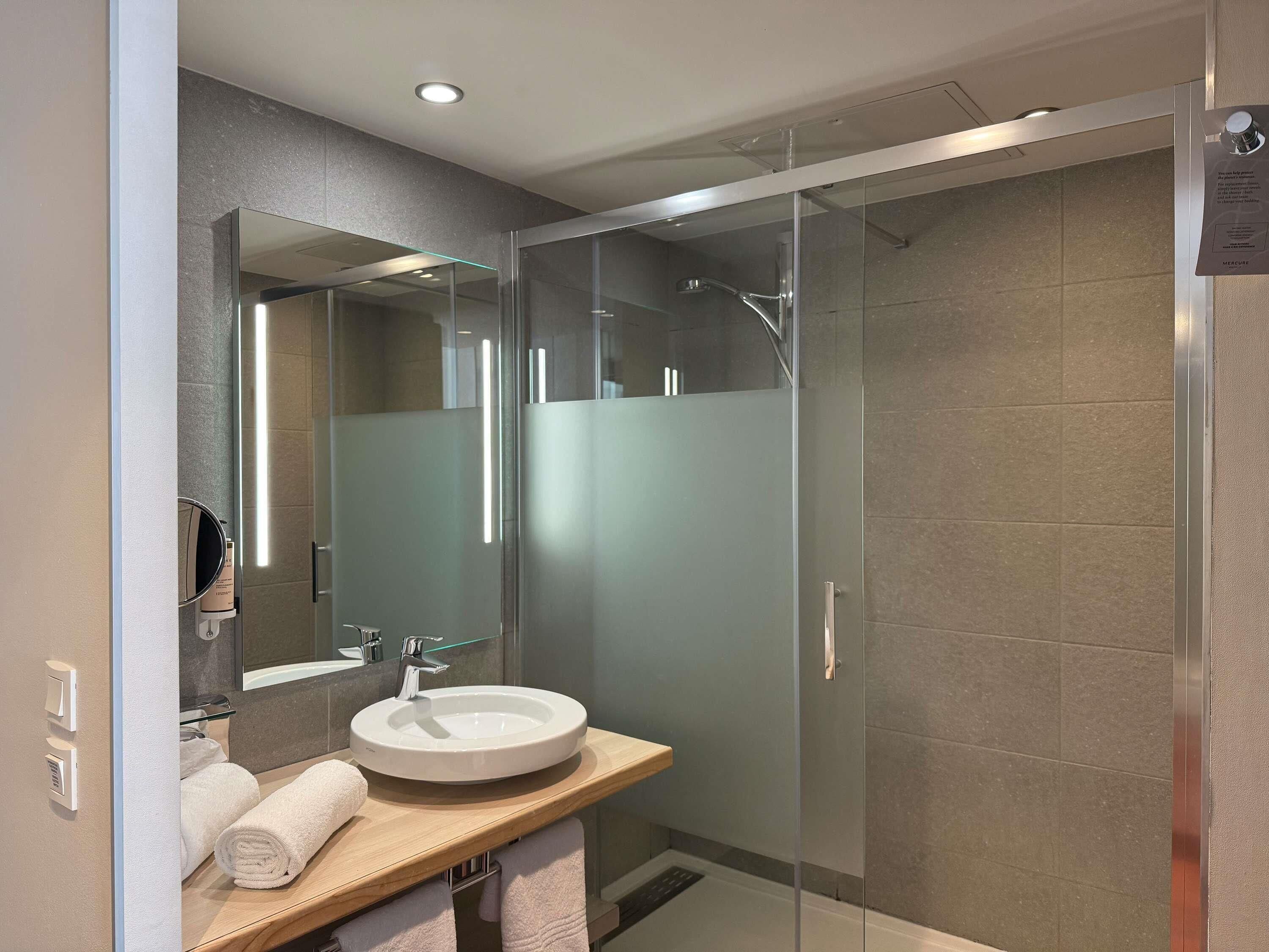 A modern bathroom with a glass-enclosed shower, a round sink, and a mirror above it.