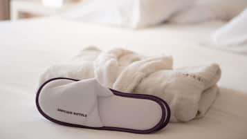 Una cama bien tendida con sábanas blancas y un detalle morado al pie.