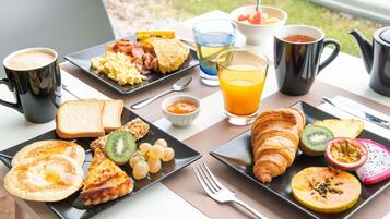 Una mesa de desayuno con tostadas, huevos, croissants y fruta. También hay tazas de café y jugo.