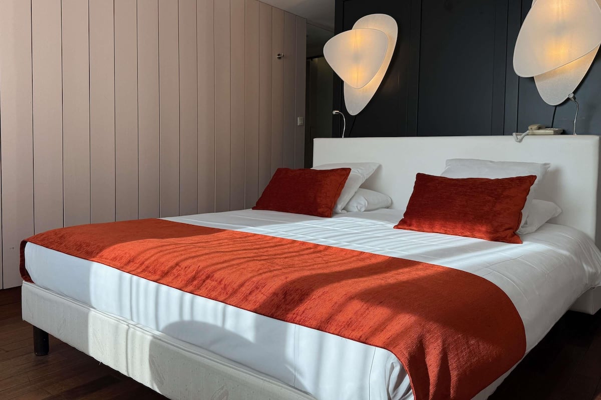 Un dormitorio moderno con una cama grande, ropa de cama blanca y dos almohadas rojas.