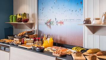 A breakfast buffet with various food items, a painting of paragliders, and kitchen utensils.