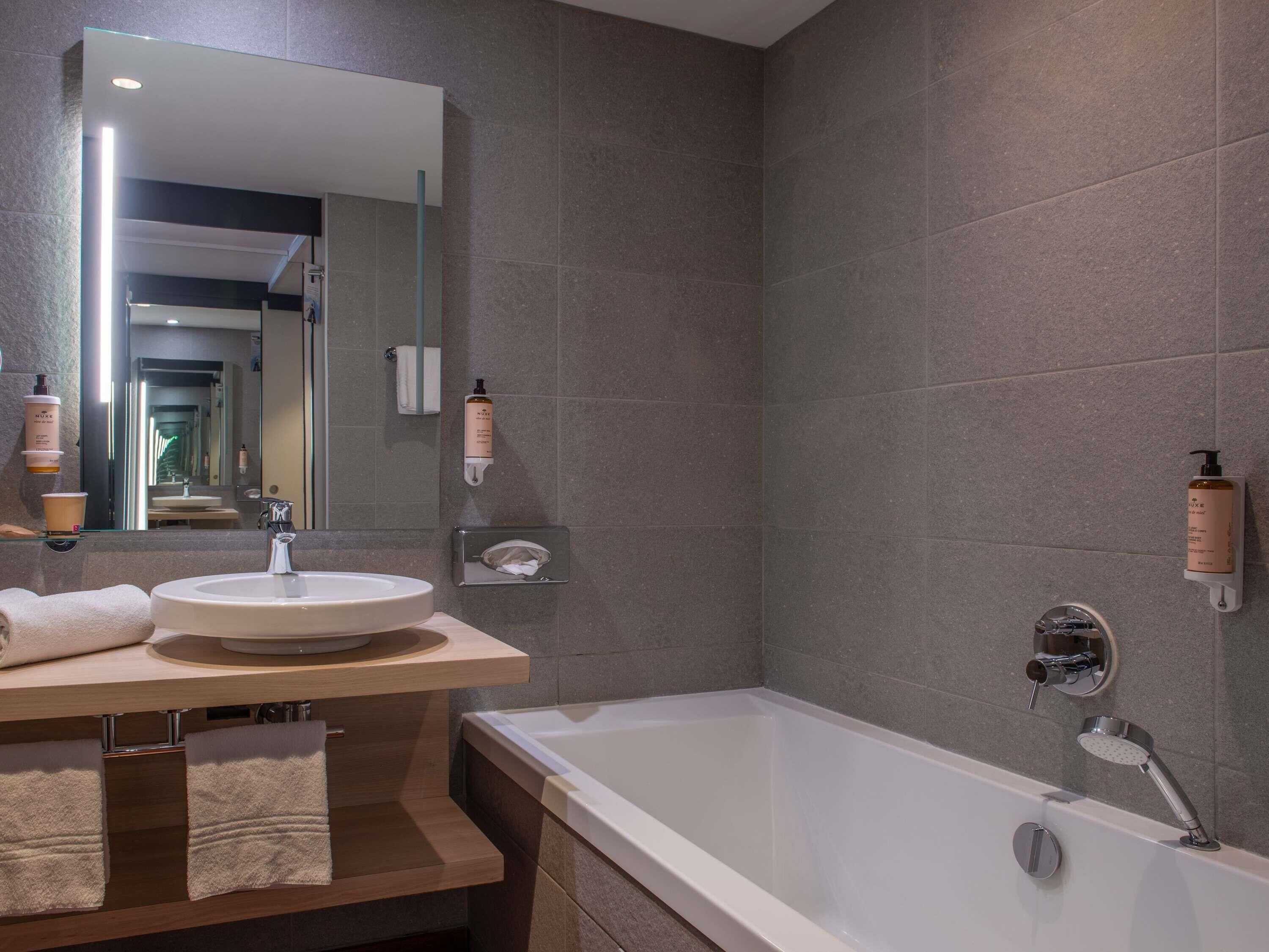 A modern bathroom with a large bathtub, a round sink, and a mirror above the sink.