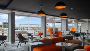 A modern lounge area with large windows, orange and grey seating, and pendant lighting. - Mercure Dieppe La Présidence (Dieppe)
