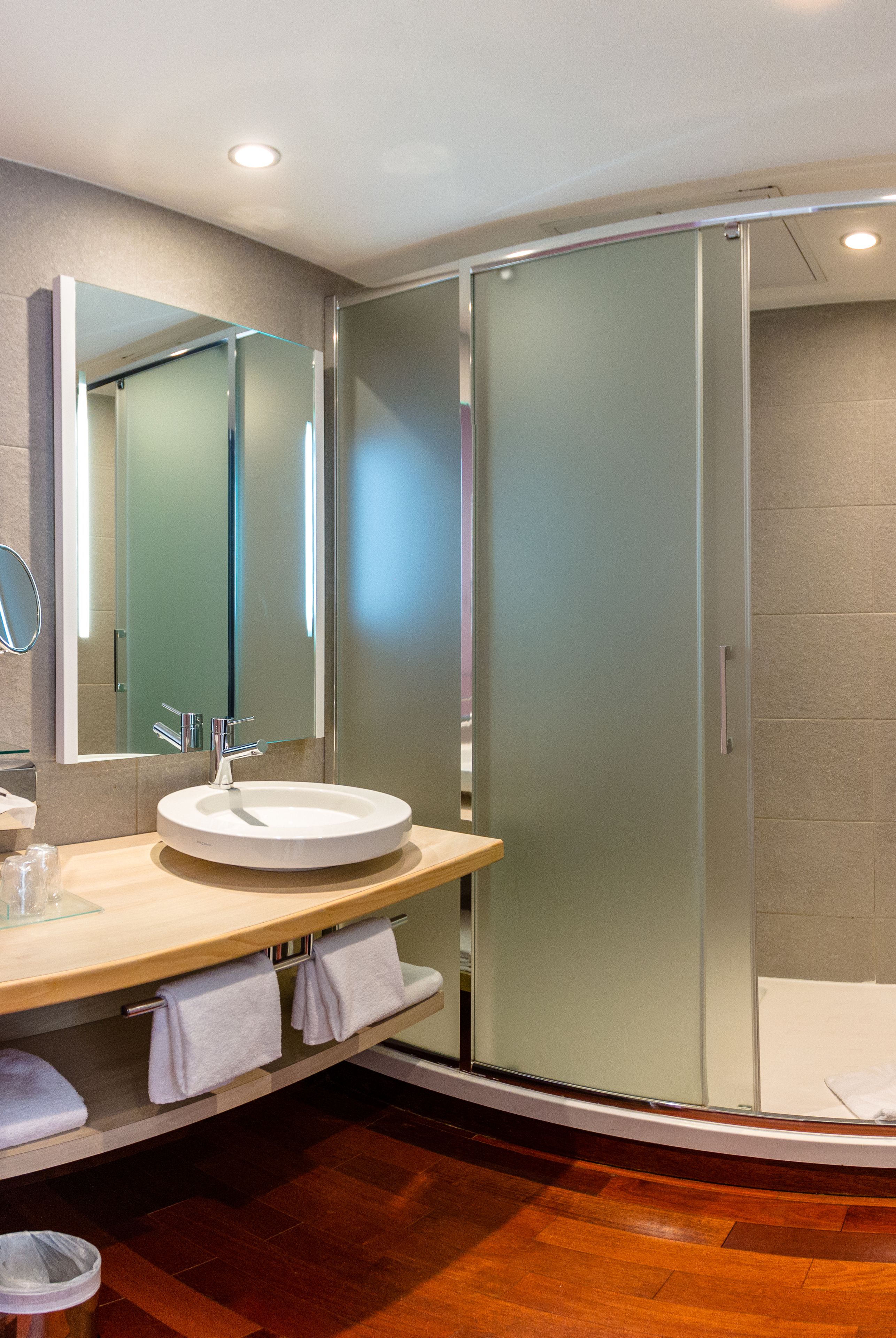 Un baño moderno con un lavabo redondo, un espejo grande y una ducha con mampara de vidrio.