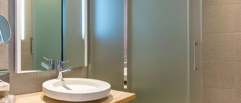 Un baño moderno con un lavabo redondo, un espejo grande y una ducha con mampara de vidrio.