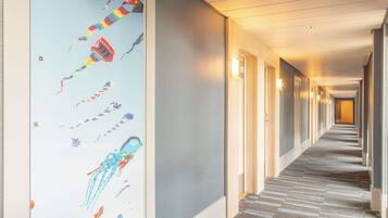 Een hotelhal met een tapijtvloer, deuren aan één kant en een muur met een kleurrijke muurschildering.
