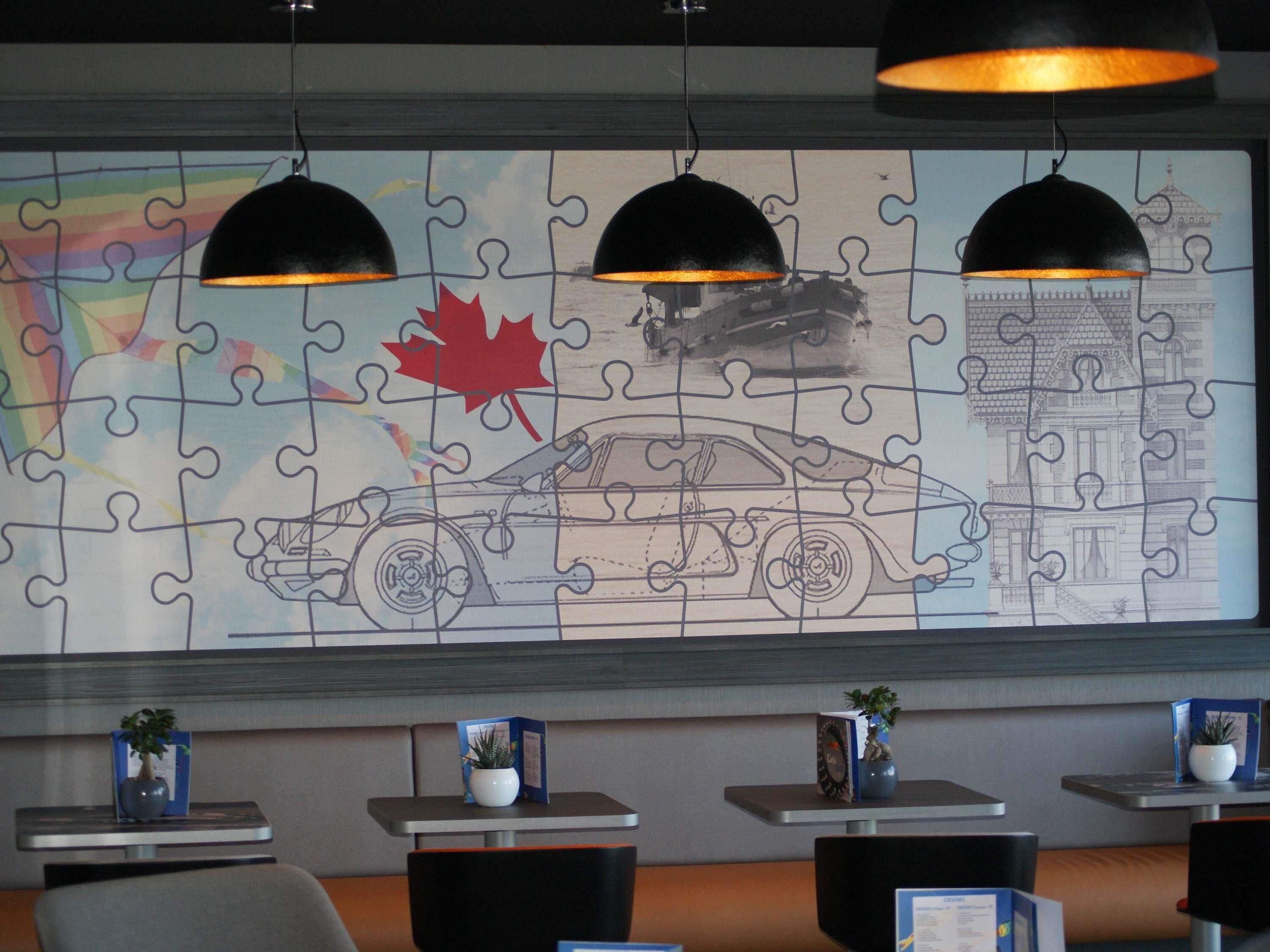 A puzzle wall with a car and a building, tables with potted plants, and pendant lighting.