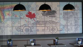 A puzzle wall with a car and a building, tables with potted plants, and pendant lighting.