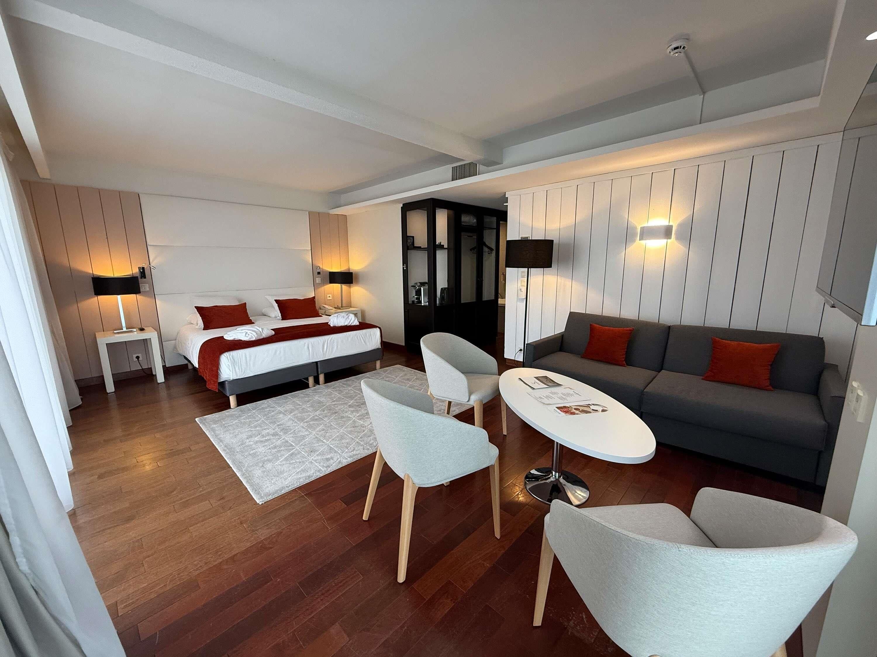 A modern hotel room with a bed, a sofa, two armchairs, a small table, and a desk.