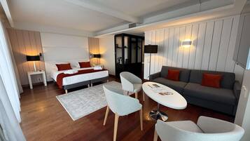 A modern hotel room with a bed, a sofa, two armchairs, a small table, and a desk.