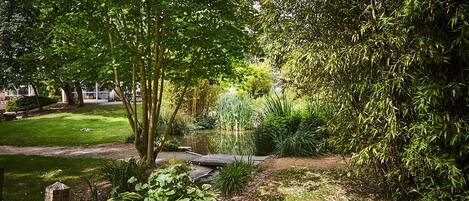 A serene garden with a pond, lush greenery, and a wooden bridge.