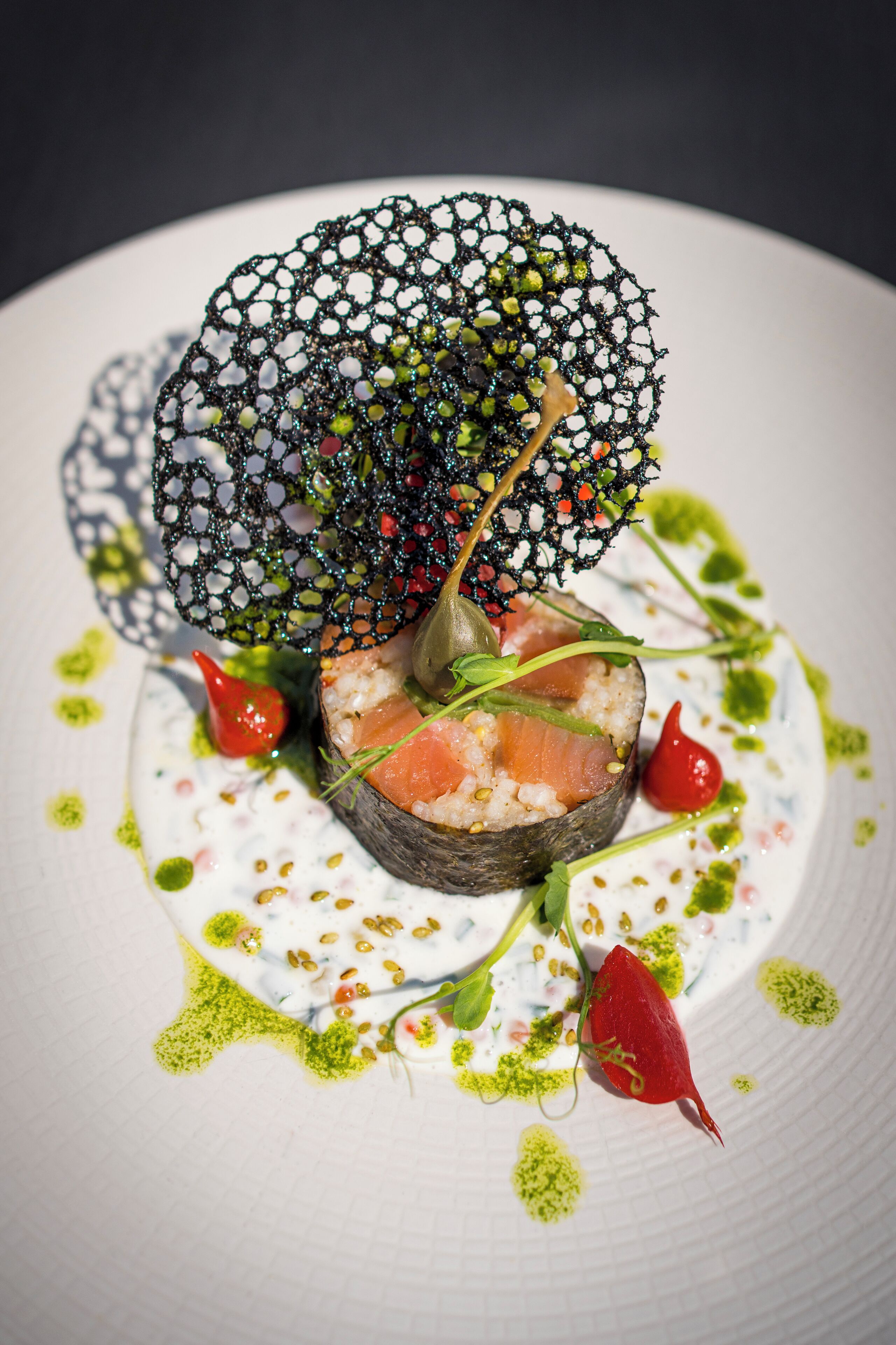A plate with a sushi dish, green sauce, and a decorative leaf.