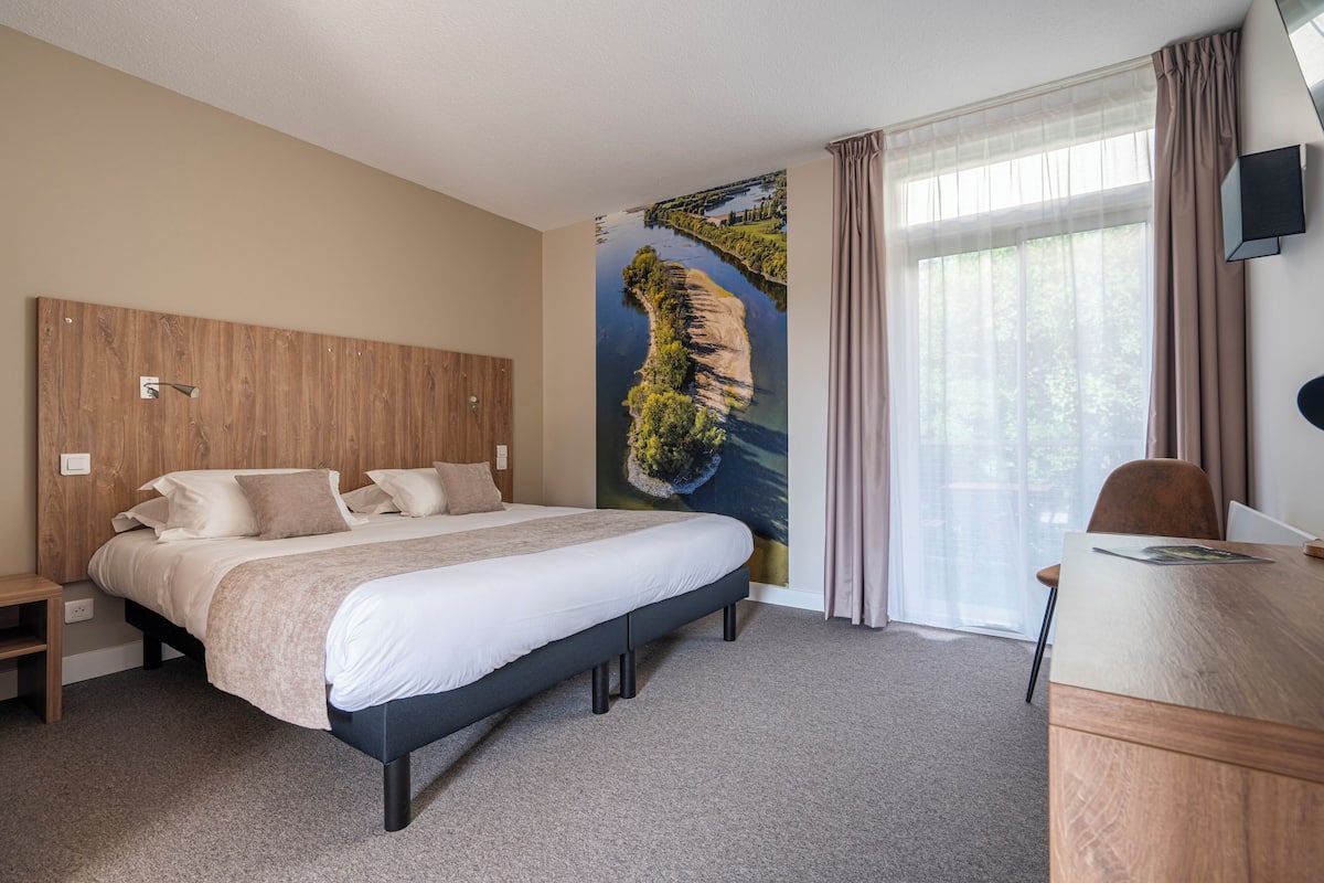 A modern hotel room with a large bed, a desk, and a scenic mural on the wall.