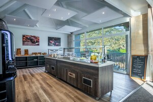 Cozinha moderna com ilha central, soalho de madeira e grandes janelas com vista para o verde.