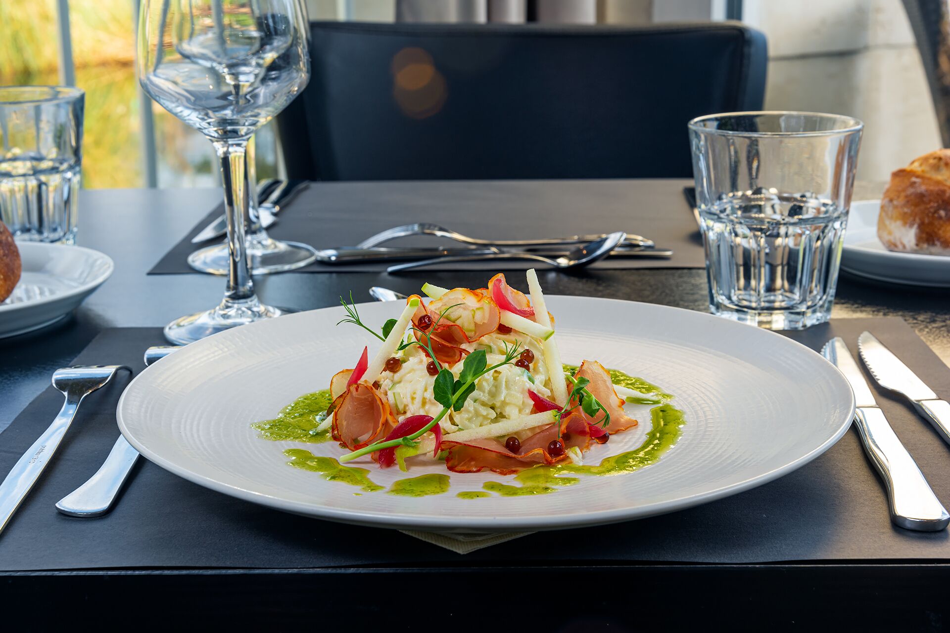 A plate of food with a green sauce, accompanied by a glass of water and a glass of wine on a table.