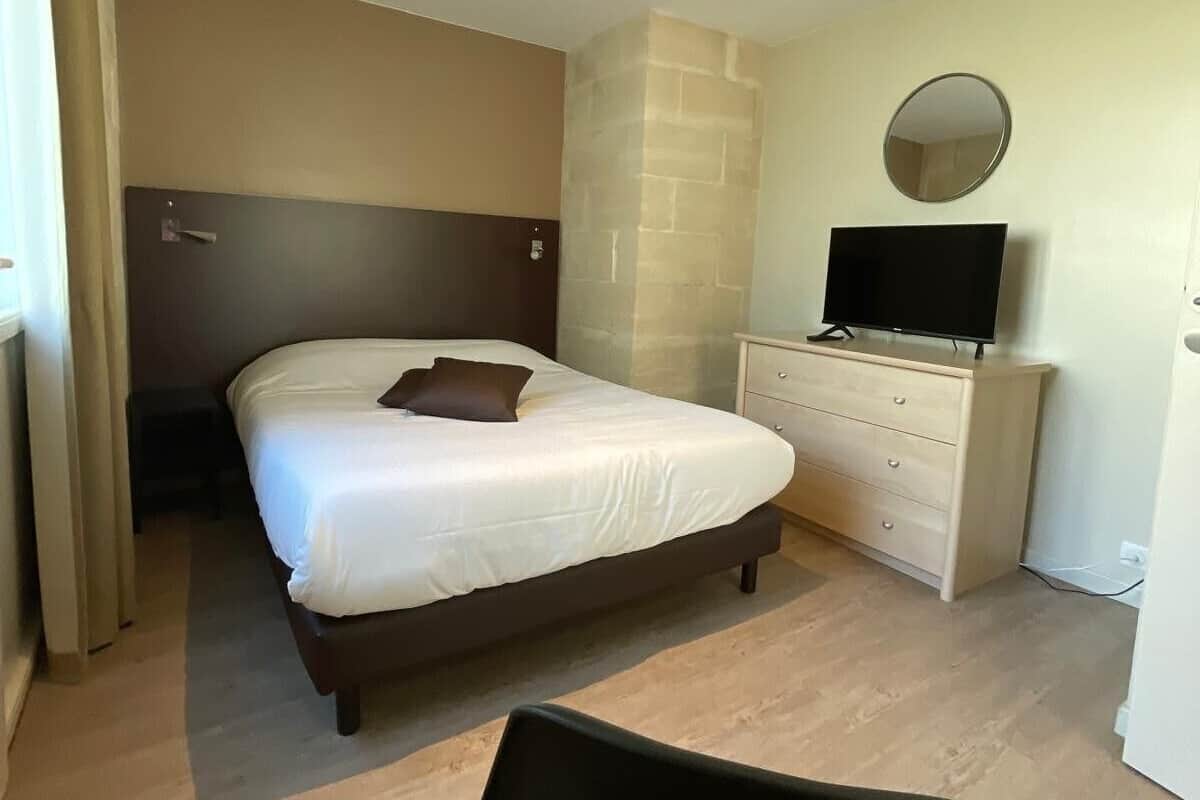 A hotel room with a bed, a dresser, a TV, and a chair.