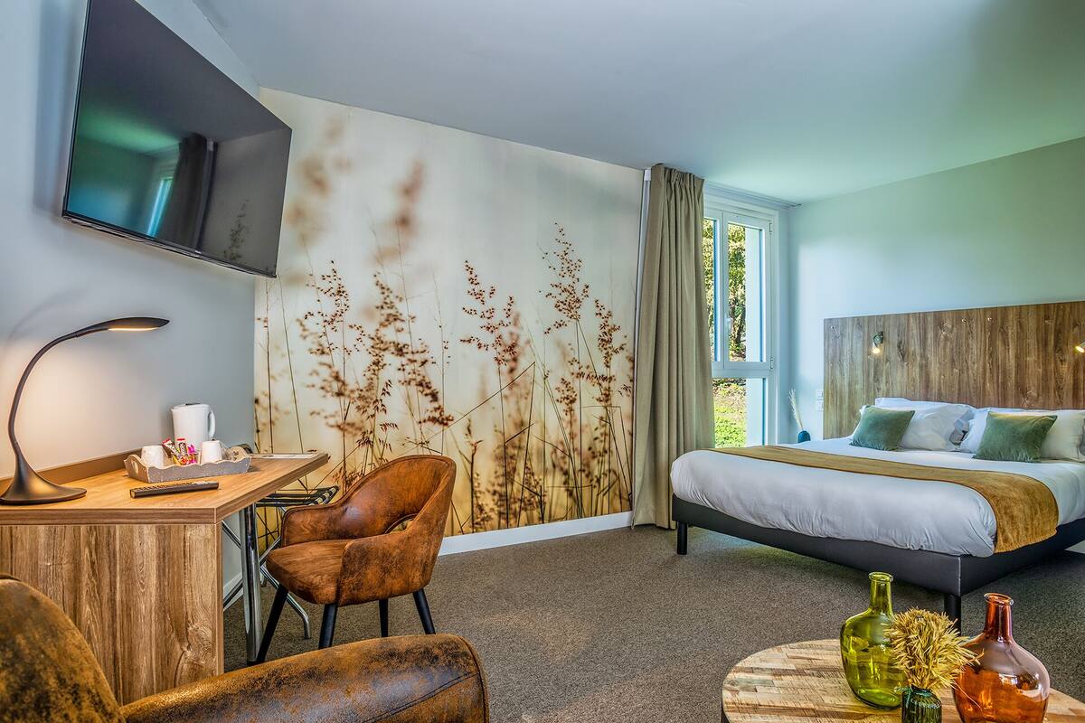 A hotel room with a bed, a desk with a lamp, a chair, and a wall with a nature-themed mural.