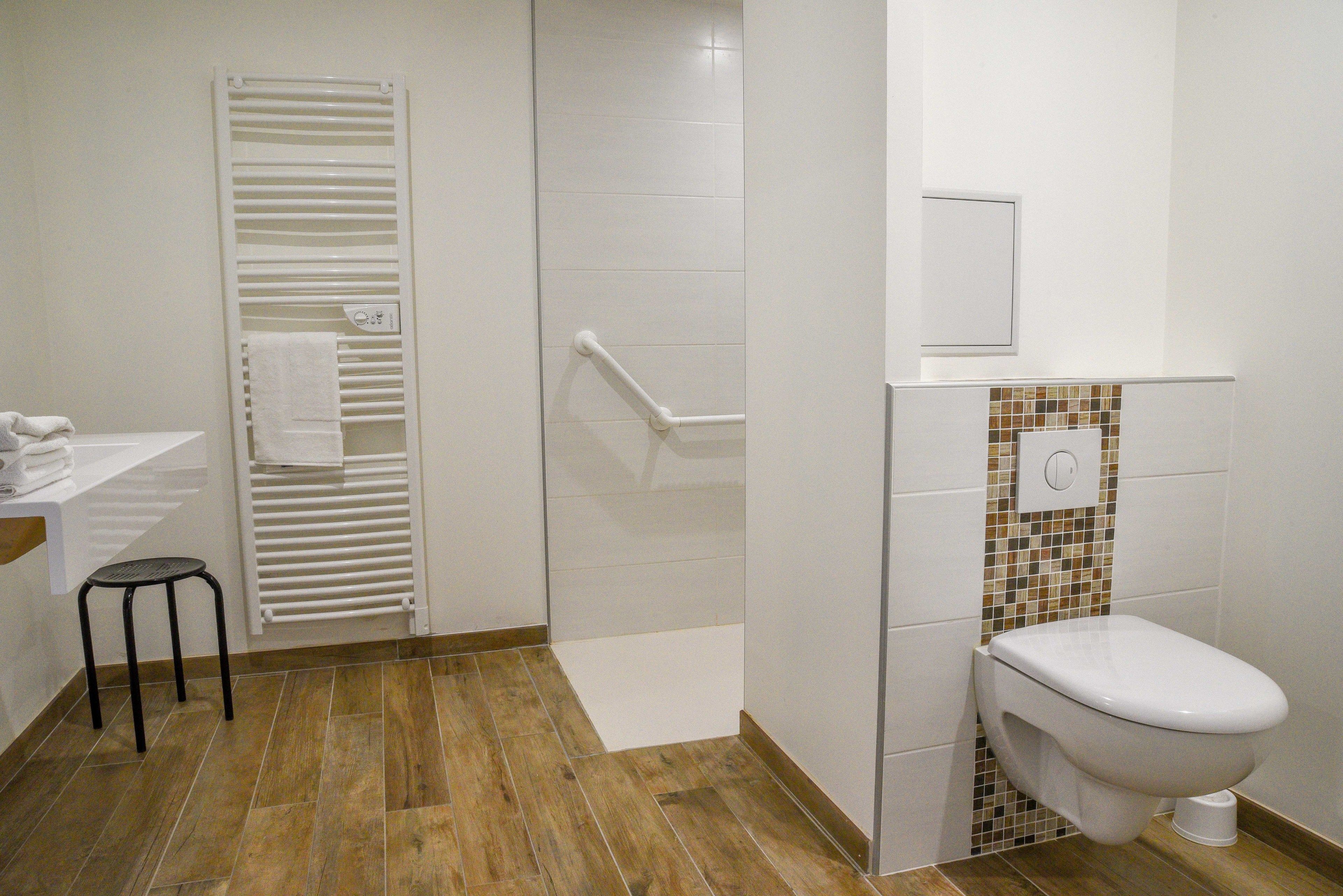 A bathroom with a toilet, a shower with a white towel rack, and a small stool.