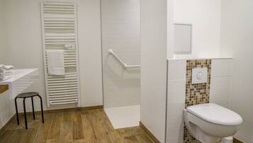 A bathroom with a toilet, a shower with a white towel rack, and a small stool.
