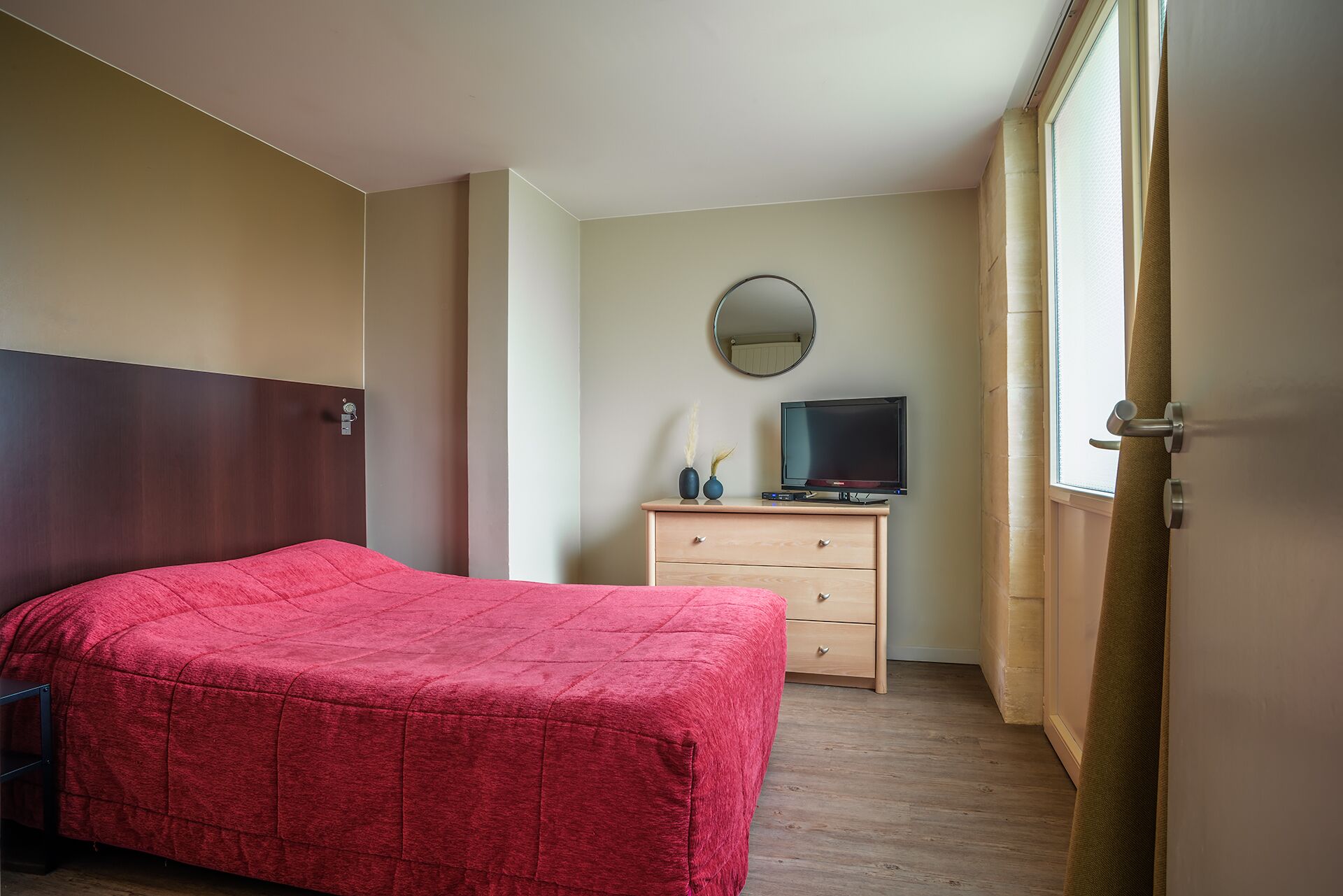 Ein Hotelzimmer mit Bett, Schminktisch, Fernseher und Fenster.