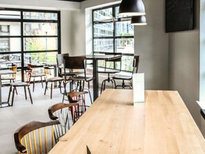 A spacious cafe with multiple tables and chairs, large windows, and a modern pendant light. - ibis Styles Clermont-Ferrand République (Clermont-Ferrand)