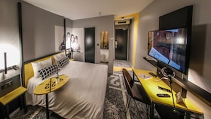 Habitación de hotel con cama, mesitas de noche, escritorio con silla, televisor y espejo.
