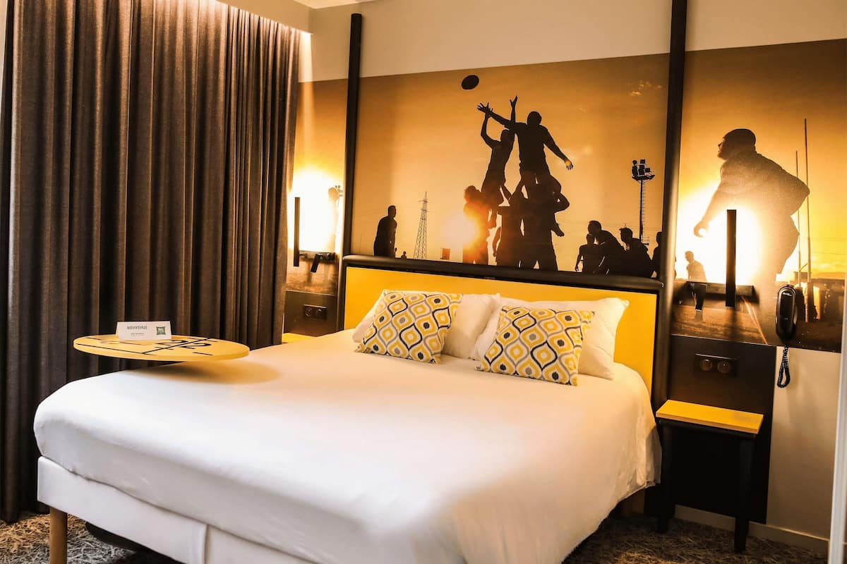 Habitación de hotel con una cama grande, una mesita de noche con lámpara y una pared decorada con un diseño silueta.
