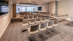 Un salón de conferencias con filas de sillas, una pantalla de proyector y un gran ventanal.