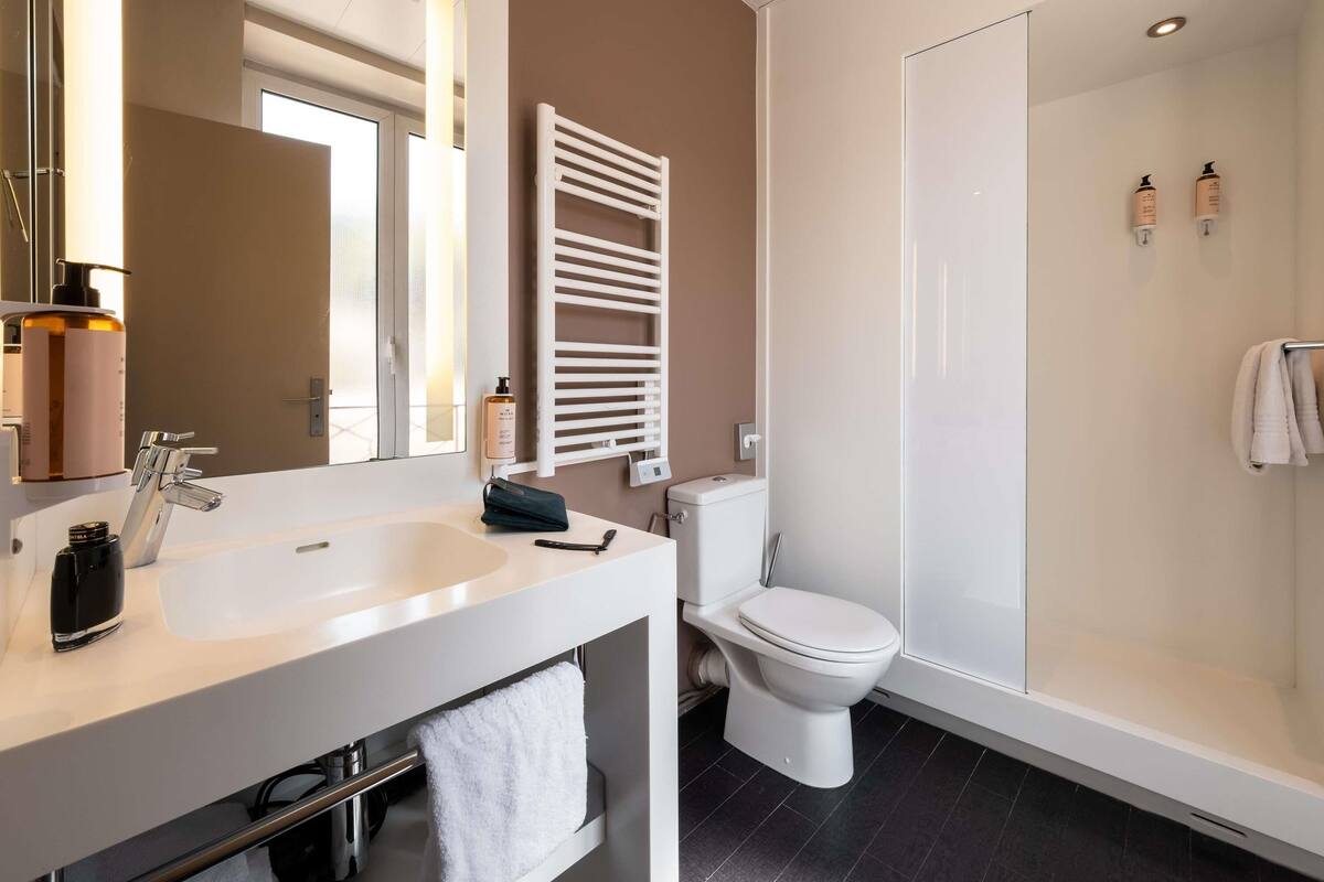 A modern bathroom with a white sink, a toilet, a shower, and a towel rack.