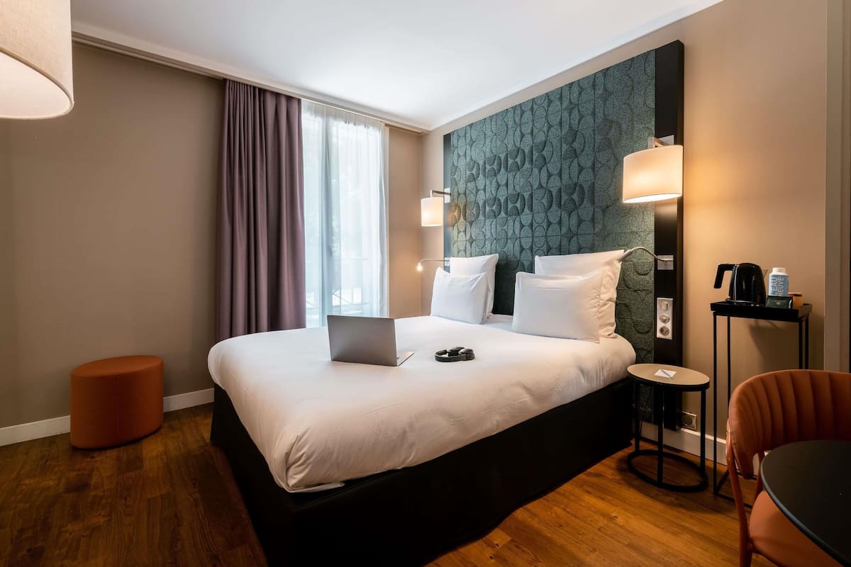 A hotel room with a bed, a laptop, a coffee machine, and a chair.
