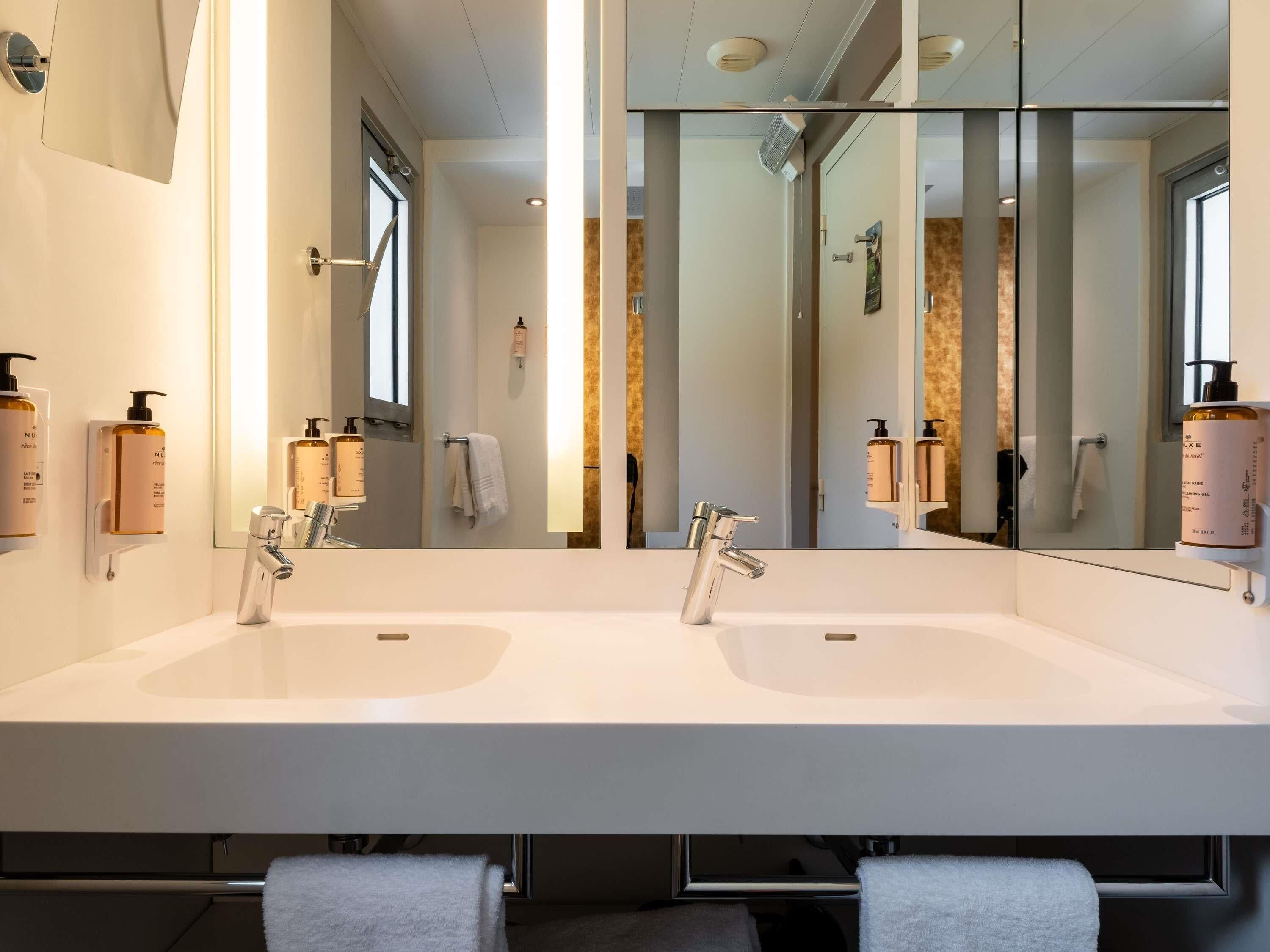 Un baño moderno con dos lavamanos, un espejo grande y un perchero para toallas.