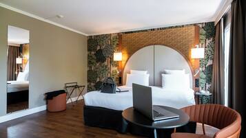 A hotel room with a bed, a laptop on a small table, a chair, and a trash bin.
