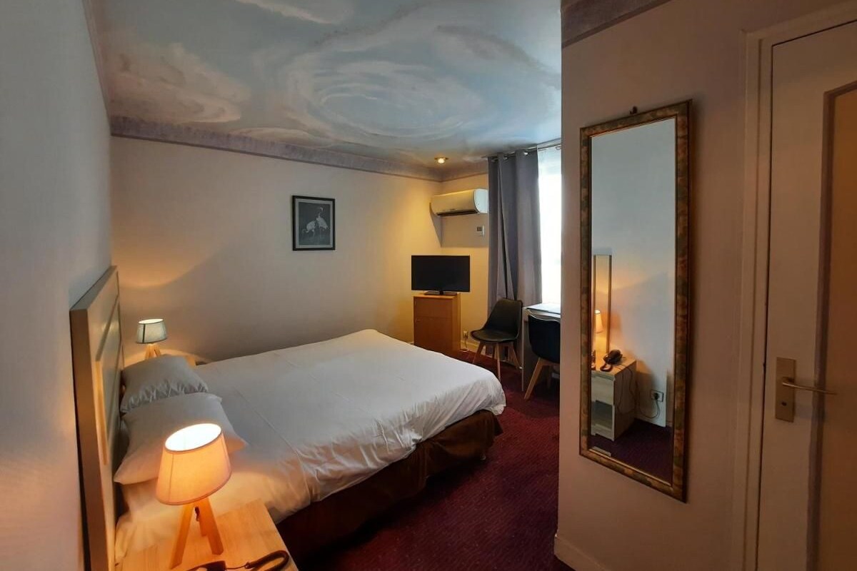 Ein Hotelzimmer mit Bett, Nachttischlampe, Fernseher, Schreibtisch, Stuhl und einem Spiegel an der Wand.