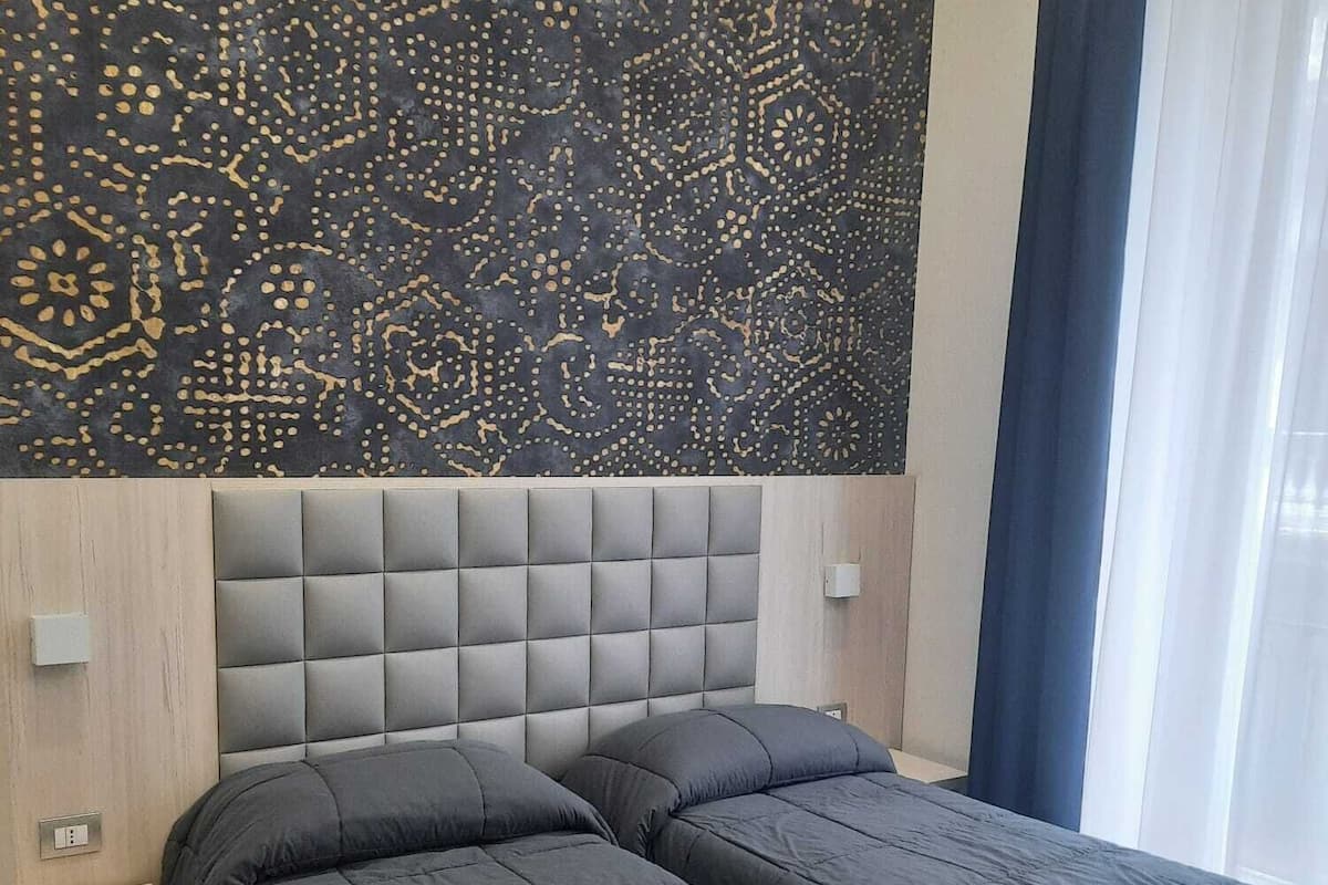 Una habitación con dos camas, un papel tapiz estampado y una ventana con cortinas.
