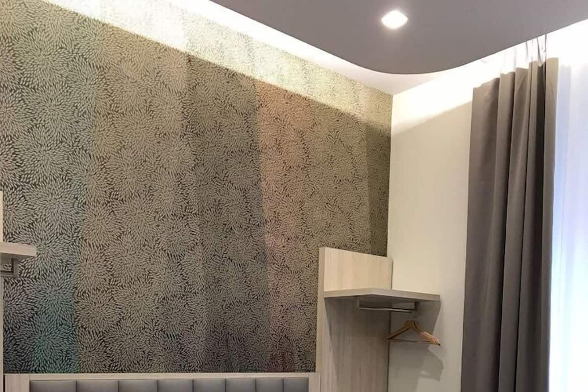 Habitación de hotel con cama, mesita de noche, estante en la pared y ventana con cortinas.