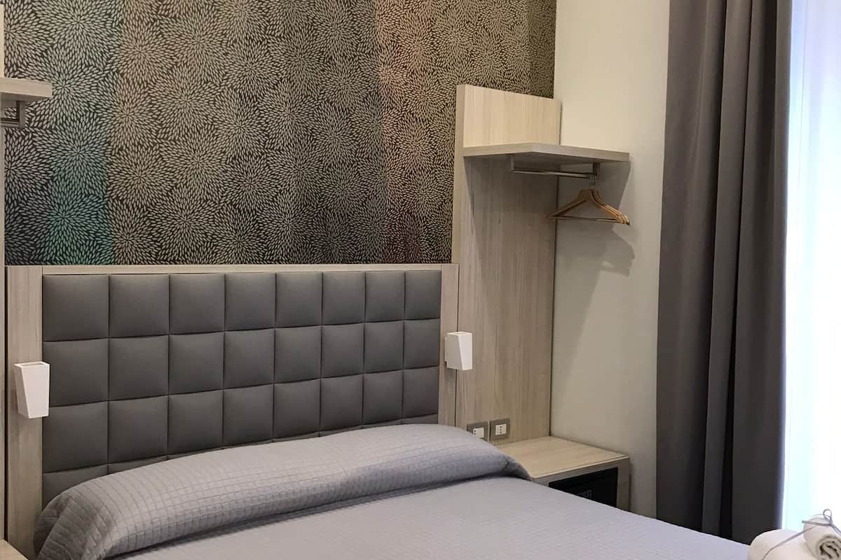 Una cama bien hecha con cabecera gris y pared con textura al fondo.